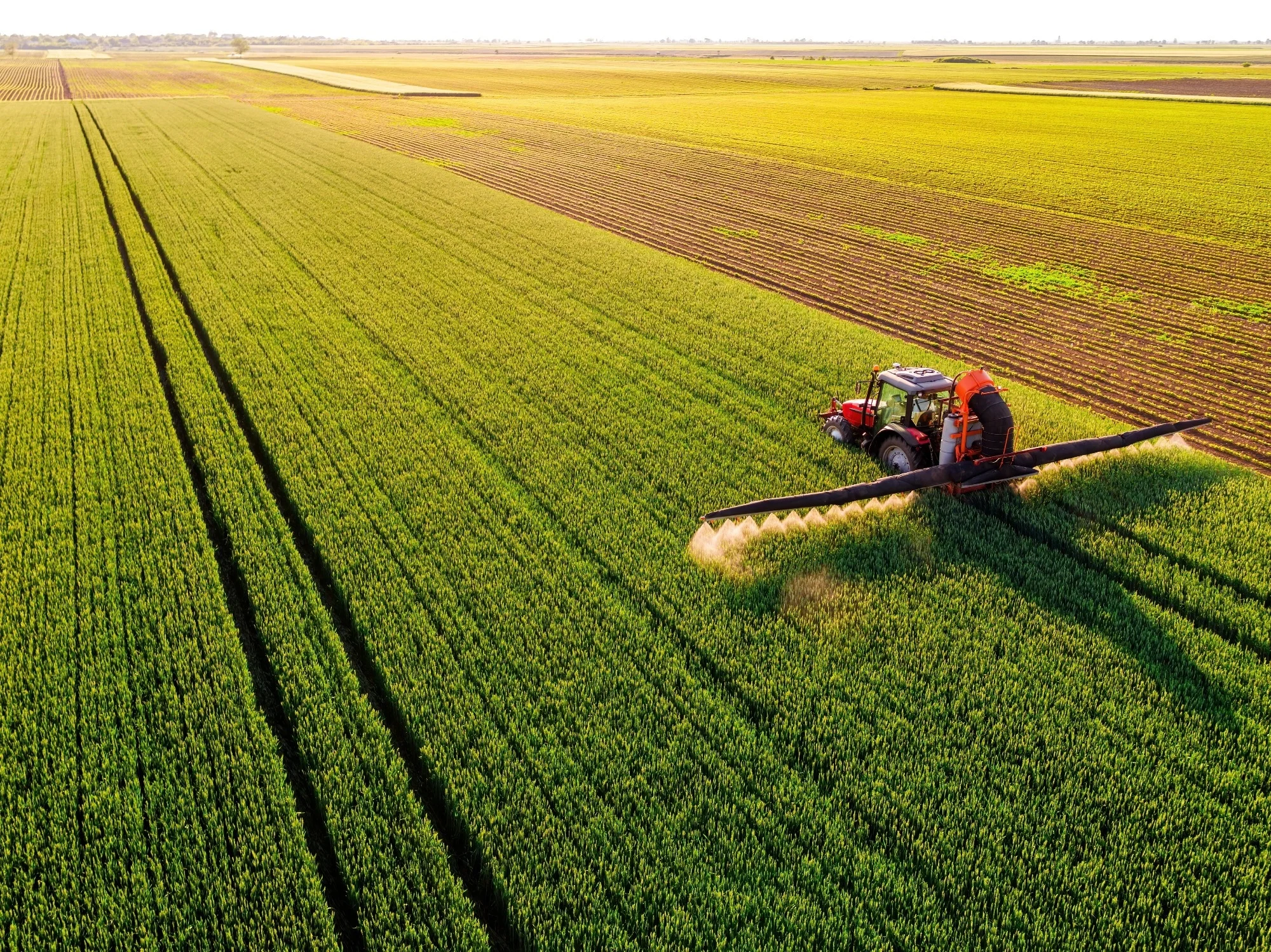 Agricultural Equipment - Modern farming with tractor spraying crops in vast green fields